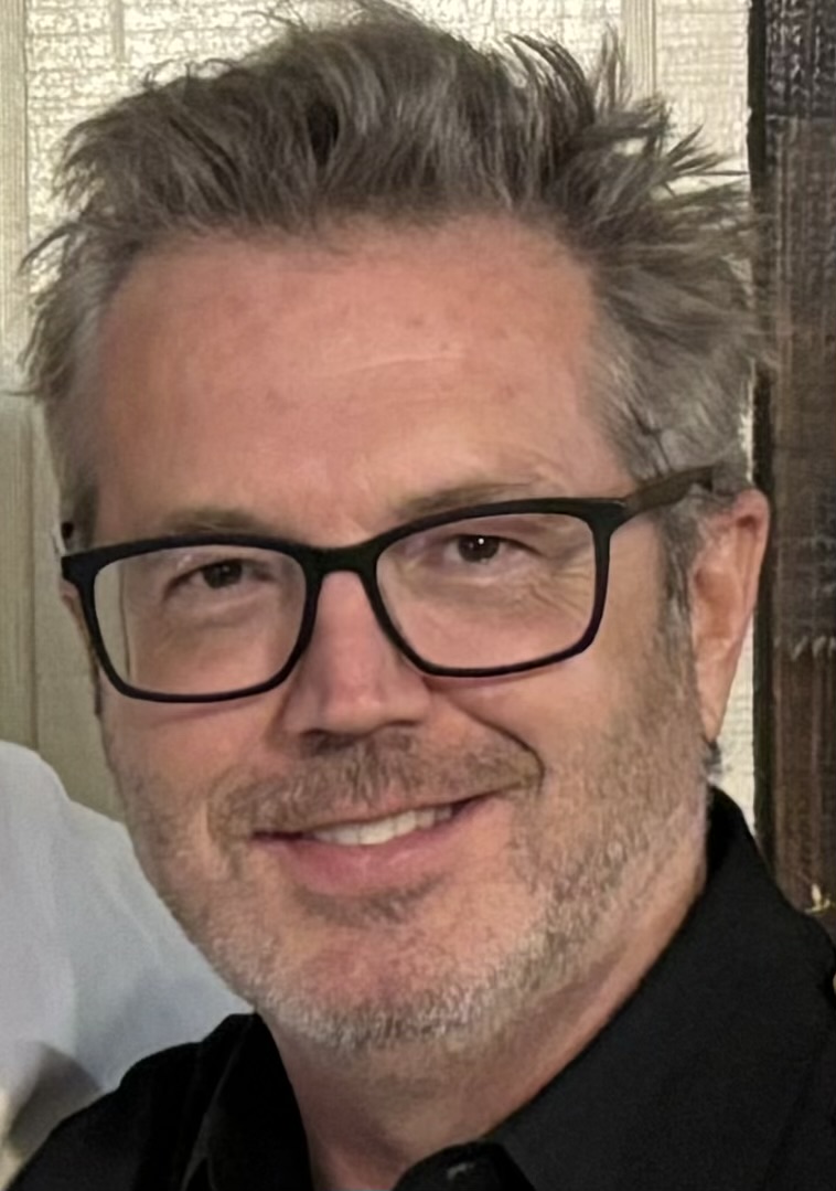 Smiling man with gray hair and black-framed glasses, wearing a dark shirt. - Breck Film | Eclipse Theater